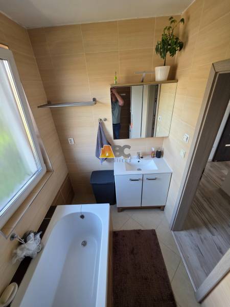 Ein Badezimmer in einem Einfamilienhaus mit einer Badewanne, einem Waschbeckenunterschrank und einem Fenster mit Licht.