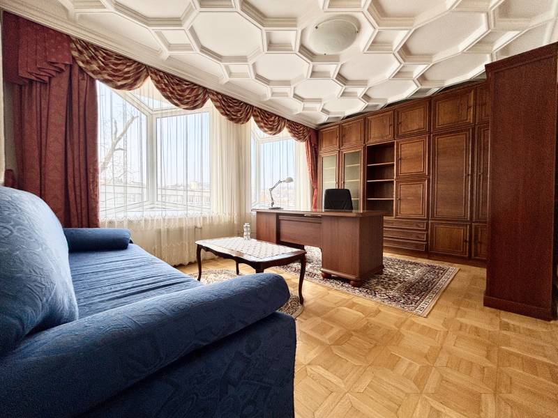 Ein Zimmer in einer 4-Zimmer-Wohnung mit einem bequemen Sofa, einem Schreibtisch und einem Boden in Holzoptik.