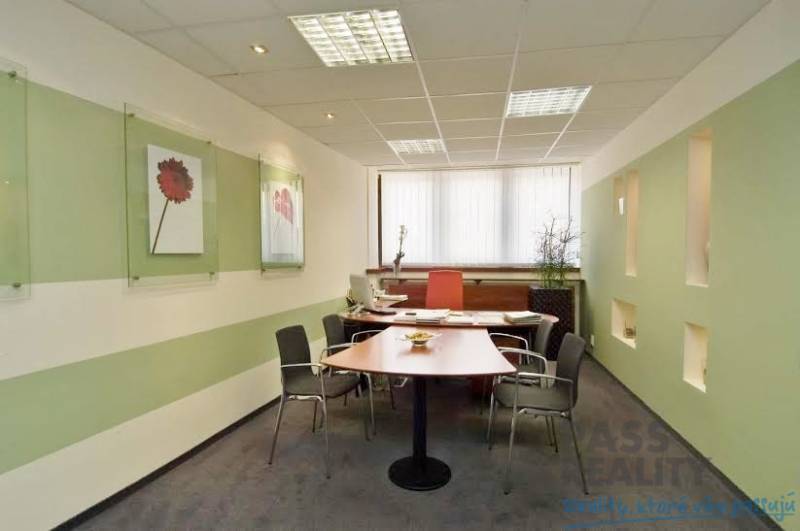 Büros mit Schreibtisch, Stühlen, an den Wänden angebrachten Dekorationen und einem Fenster mit vertikalen Jalousien.