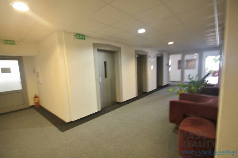 Innenraum eines Büros mit Aufzügen und Sofa, weiße Wand, Piktogramme „EXIT“.