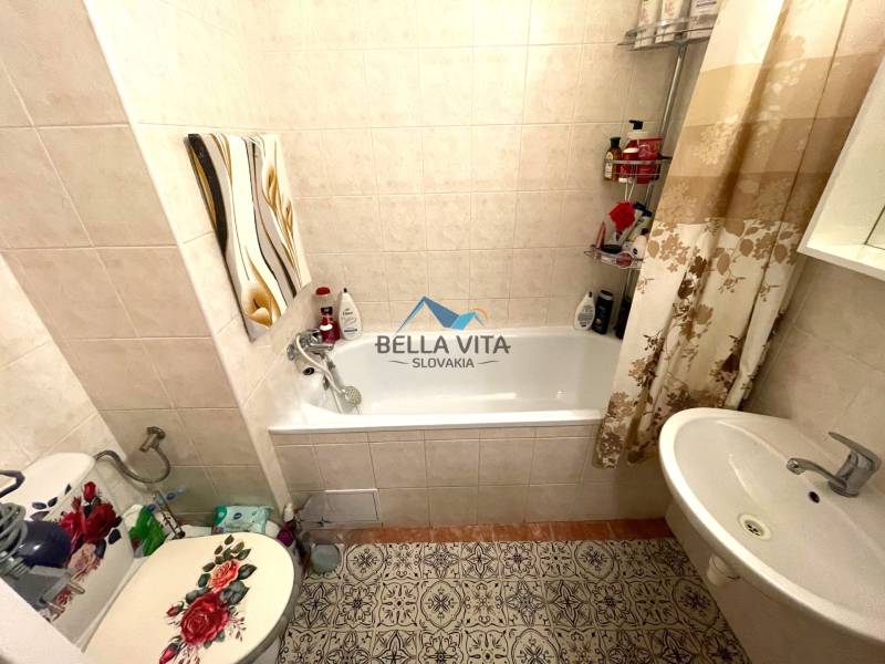 Badezimmer in einer Einzimmerwohnung mit Badewanne, Waschbecken und verziertem WC-Sitz.