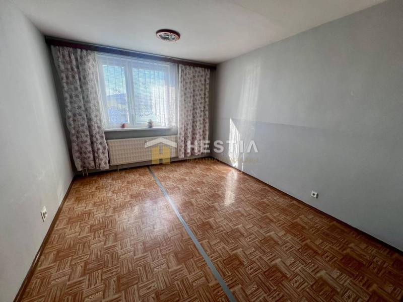 Ein Zimmer in einer 3-Zimmer-Wohnung mit einem Boden in Holzoptik und hellgrauen Wänden.