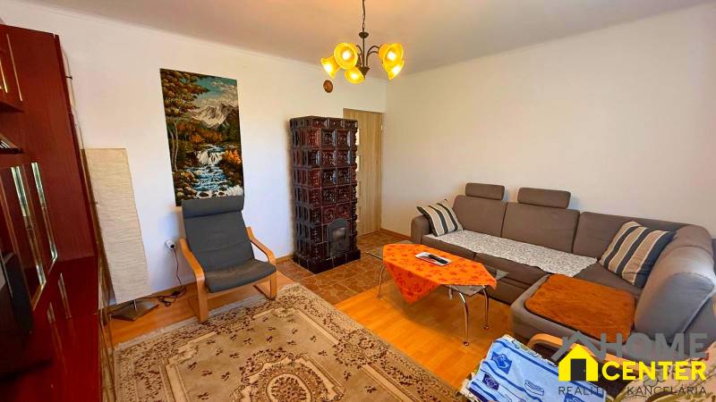 Wohnzimmer in einem Einfamilienhaus mit Sofa, Sessel, Kachelofen und einem Naturbild.