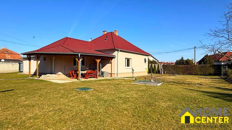 Ein Einfamilienhaus in Zemianska Olča mit rotem Dach und Holzunterstand, grasbewachsener Garten.