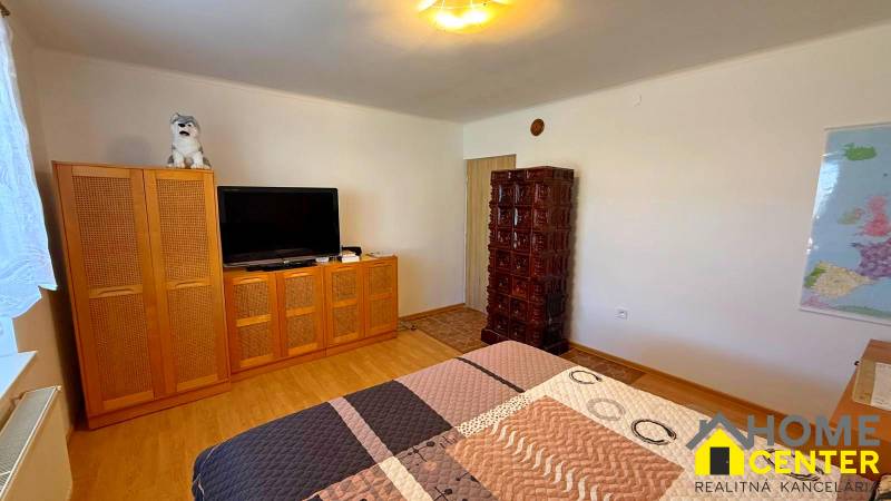 Ein Zimmer in einem Einfamilienhaus mit einem Fernseher, einem Schrank, einem Kachelofen und einem Boden mit Holzdekor.