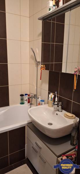 Badezimmer mit Dusche, Waschbecken und Schrank in einer 4-Zimmer-Wohnung, überwiegend dunkle Fliesen.