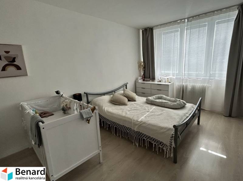 Schlafzimmer in einer 2-Zimmer-Wohnung mit Kinderbett, Bett und Kommode, Boden mit Holzdekor.