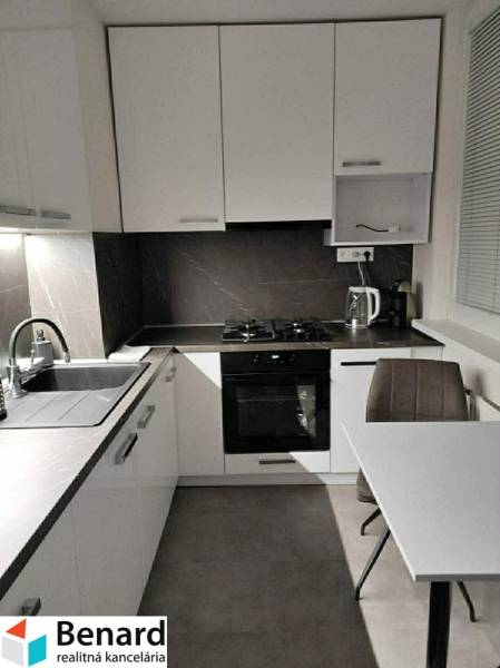 Küche mit weißen Schränken und einem Tisch in einer Zweizimmerwohnung mit Holzboden.