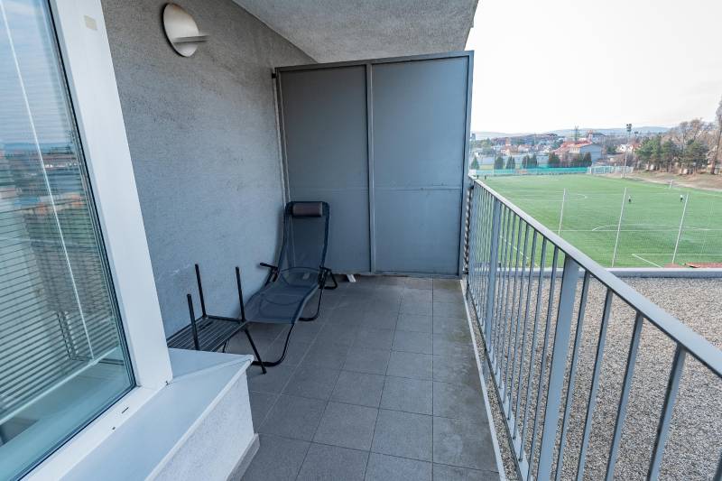 Balkon einer 2-Zimmer-Wohnung mit Blick auf den Fußballplatz und einer Liege.