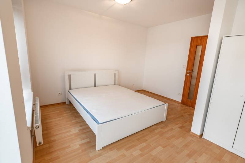 Schlafzimmer in einer 2-Zimmer-Wohnung mit einem weißen Bett und einem Boden in Holzoptik.