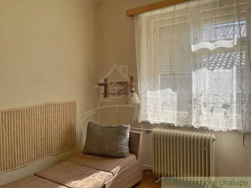 Einfaches Zimmer in einem Einfamilienhaus mit einer Liege und dekorativen Vorhängen am Fenster.