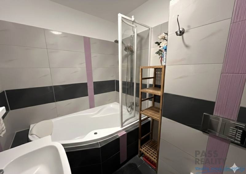 Badezimmer in einer 2-Zimmer-Wohnung mit Eckbadewanne, Fliesen und Handtuchhalter.