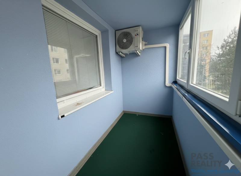 Veranda mit Verglasung und Klimaanlage in einer 2-Zimmer-Wohnung, ausgestattet mit Jalousien und grünem Teppich.