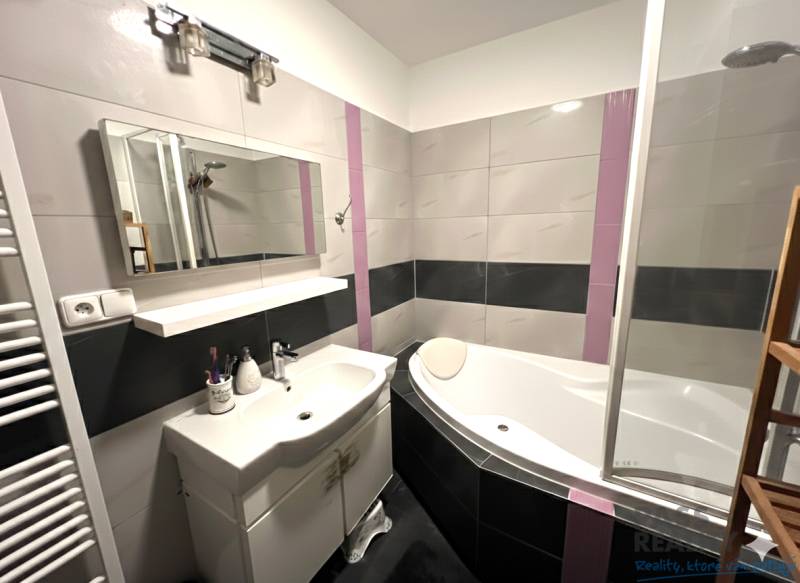 Badezimmer mit Badewanne, Waschbecken und Spiegel in einer 2-Zimmer-Wohnung.