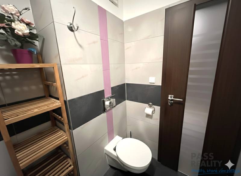 Badezimmer in einer 2-Zimmer-Wohnung mit Toilette, Holzregal und dekorativen Blumen.