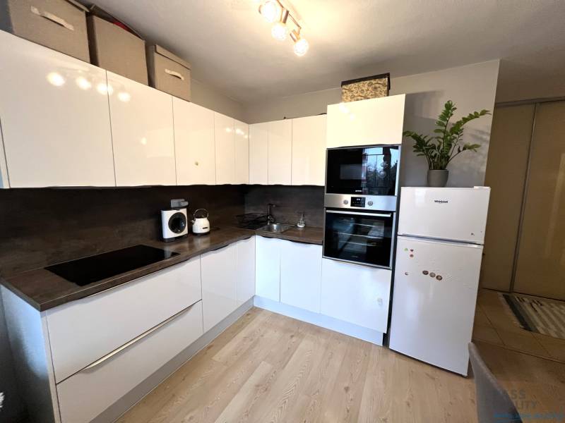 Küche in einer 2-Zimmer-Wohnung mit weißen Schränken, Geräten und einem Boden in Holzoptik.