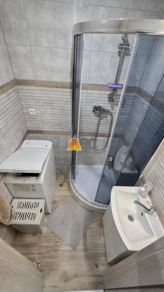 Badezimmer mit Dusche und Waschbecken in einer 2-Zimmer-Wohnung, Boden mit Holzdekor.