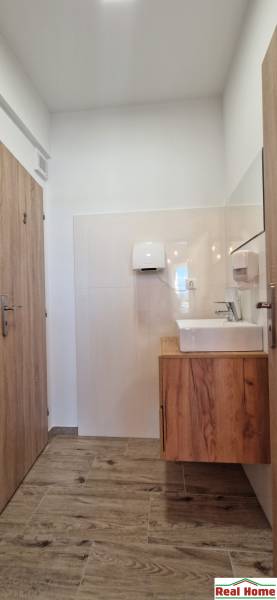 Innenraum eines Gastronomiebereichs mit hellen Wänden, einem Boden in Holzoptik und einem Waschbecken.