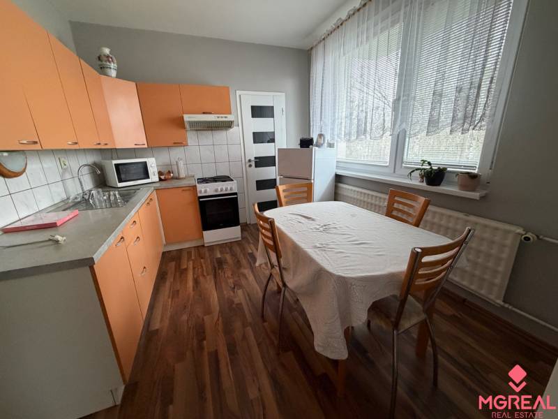 Küche mit orangefarbenen Schränken, Esstisch und Holzboden in einer 3-Zimmer-Wohnung.