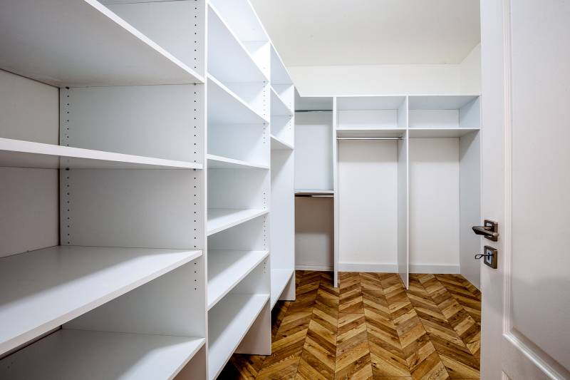 Ein Kleiderschrank mit weißen Regalen und einem Boden in Holzoptik im Ferienapartment.