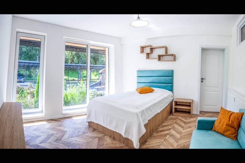 Ein helles Zimmer mit einem Bett, großen Fenstern und einem Boden in Holzoptik in einer Ferienwohnung.