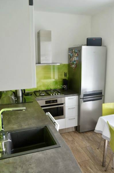 Küche in einer 2-Zimmer-Wohnung mit Edelstahlgerät, grüner Fliesenverkleidung und Holzboden.