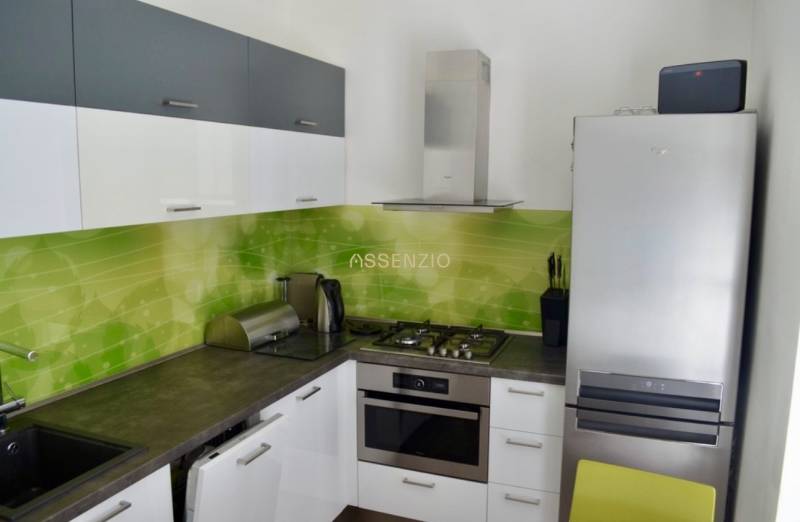 Küche mit weißen Schränken und grünen Fliesen, Gasherd und Kühlschrank in einer Zweizimmerwohnung.