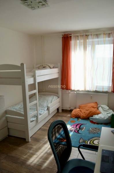 Ein Zimmer in einer 2-Zimmer-Wohnung mit einem Etagenbett, einem Schreibtisch und einem Boden in Holzoptik.