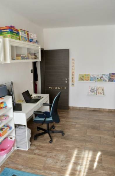 Kinderzimmer mit Tisch, Stuhl, Spielzeug und einem Boden mit Holzdekor in einer 2-Zimmer-Wohnung.