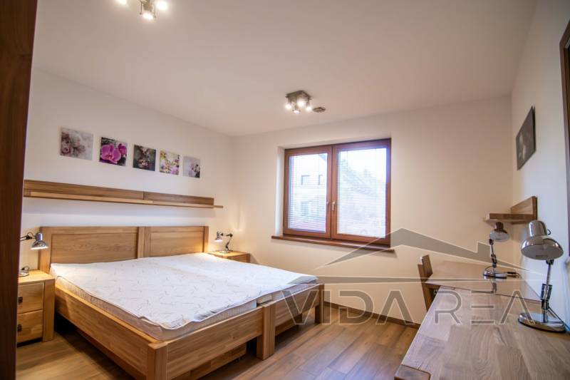 Ein Schlafzimmer in einem Einfamilienhaus mit Bett, Nachttischlampen und einem Boden in Holzoptik.