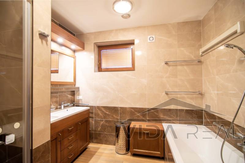 Badezimmer in einem Einfamilienhaus mit Badewanne, Waschbecken, Duschkabine und Boden mit Holzdekor.