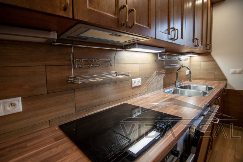 Eine Küche in einem Einfamilienhaus mit einem Boden in Holzoptik und einer Küchenzeile aus Holz.