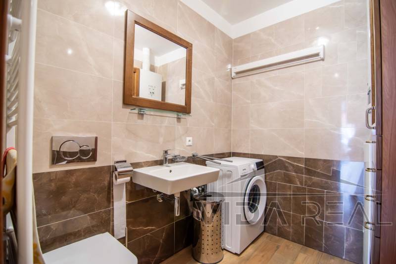 Badezimmer in einem Einfamilienhaus mit Waschmaschine, Waschbecken und Boden mit Holzdekor.