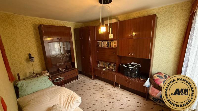 Ein Zimmer in einem Einfamilienhaus mit Möbeln, einem Bett und gemusterten Tapeten an den Wänden.