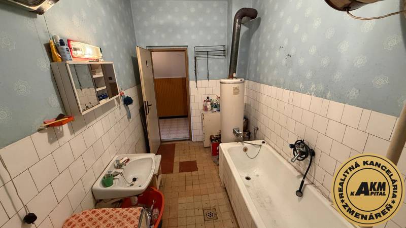 Das Badezimmer in einem Einfamilienhaus enthält eine Badewanne, ein Waschbecken, alte Möbel und einen Boiler.