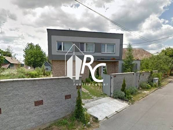 Ein Einfamilienhaus in Bystrička mit einem gepflegten Garten und einem hohen Zaun entlang der Straße.