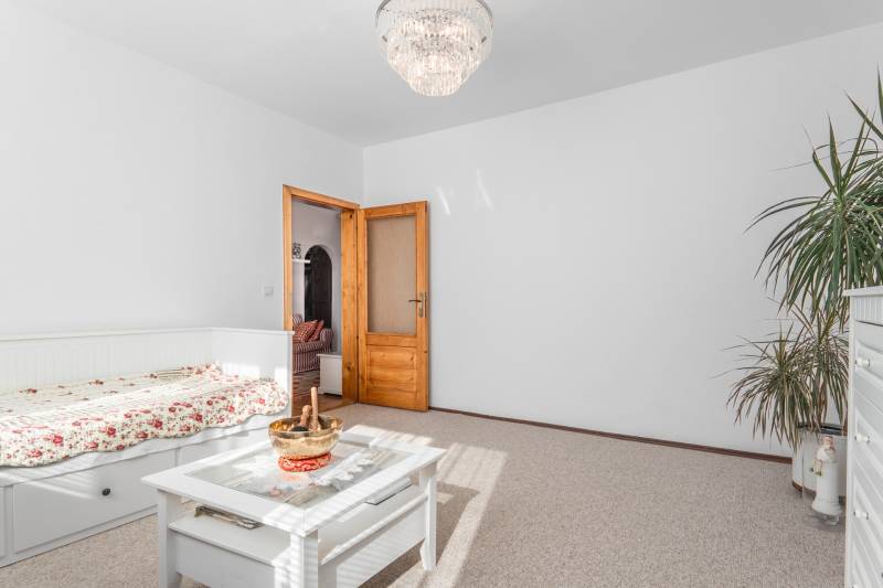 Helles Zimmer mit Blumenbettwäsche, Tisch und Kronleuchter in einer Vierzimmerwohnung.