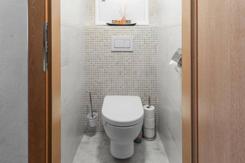 Toilette in einer 4-Zimmer-Wohnung mit gefliesten Wänden und Stauraum.