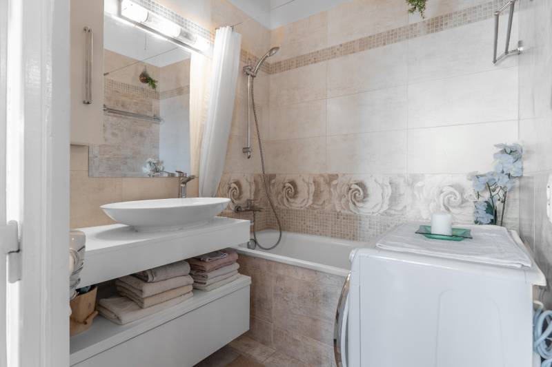 Badezimmer in einer 4-Zimmer-Wohnung mit Badewanne, Waschbecken, Waschmaschine und dekorativen Blumen.