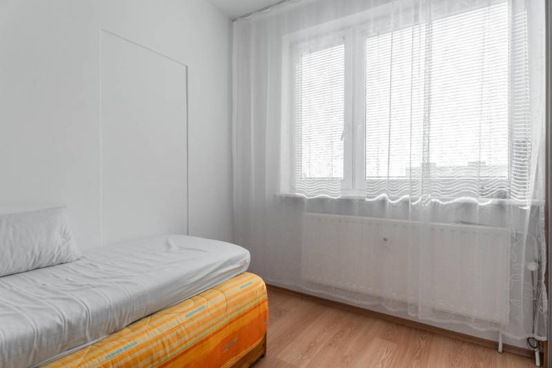 Helles Zimmer mit Bett und Fenster mit Vorhängen in einer 4-Zimmer-Wohnung.