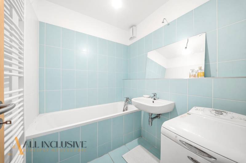 Badezimmer in einer 2-Zimmer-Wohnung mit blauen Fliesen, Badewanne und Waschmaschine.