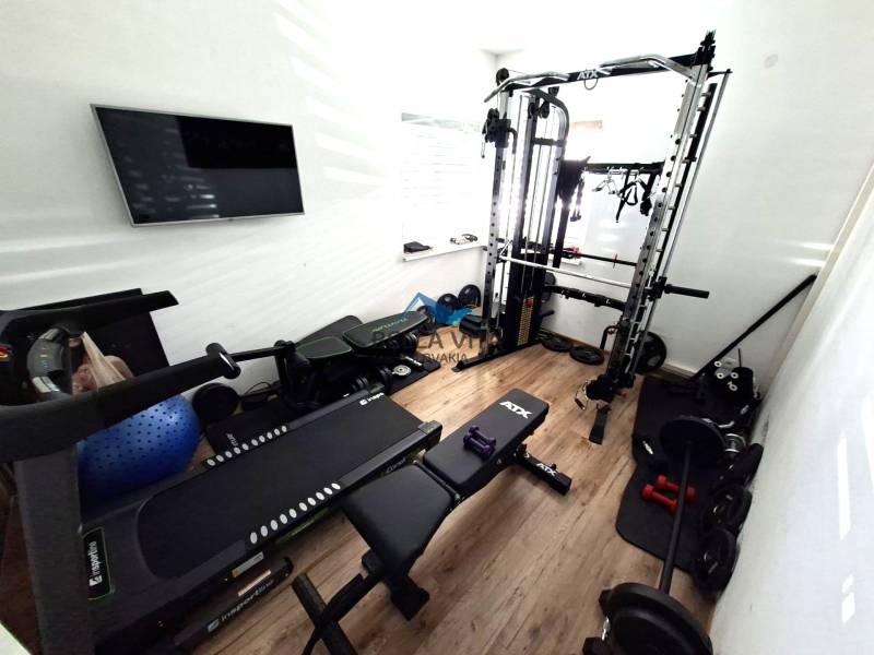 Heim-Fitnessstudio mit verschiedenen Trainingsgeräten und Bodenbelag in Holzoptik.