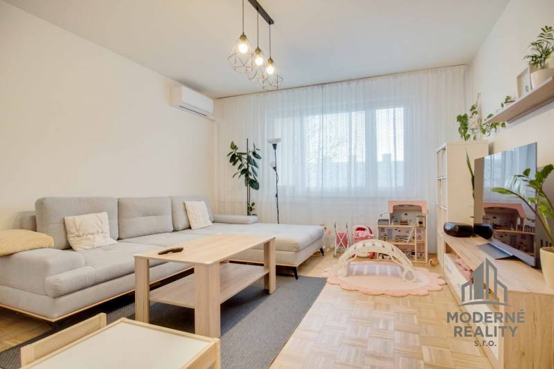 Helles Wohnzimmer in einer 3-Zimmer-Wohnung mit Holzboden und grauem Sofa.