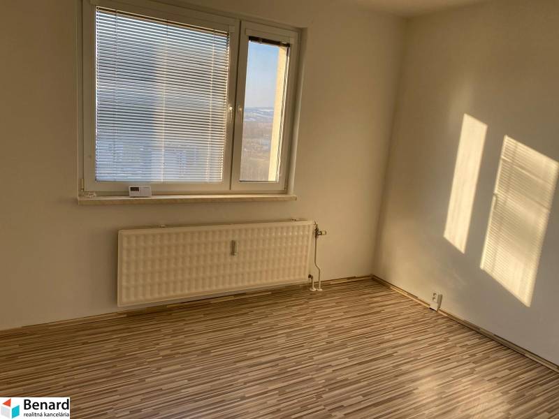 Ein Zimmer mit Fenster, Jalousien, Heizkörper und einem Boden mit Holzdekor in einer 3-Zimmer-Wohnung.