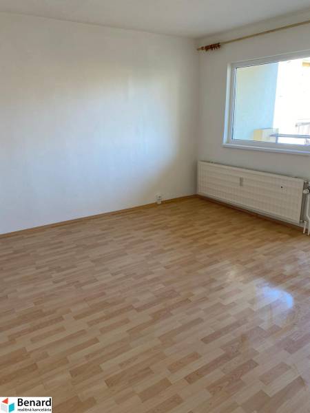 Ein Zimmer mit einem Holzboden in einer 3-Zimmer-Wohnung, helle Wand, Heizkörper.