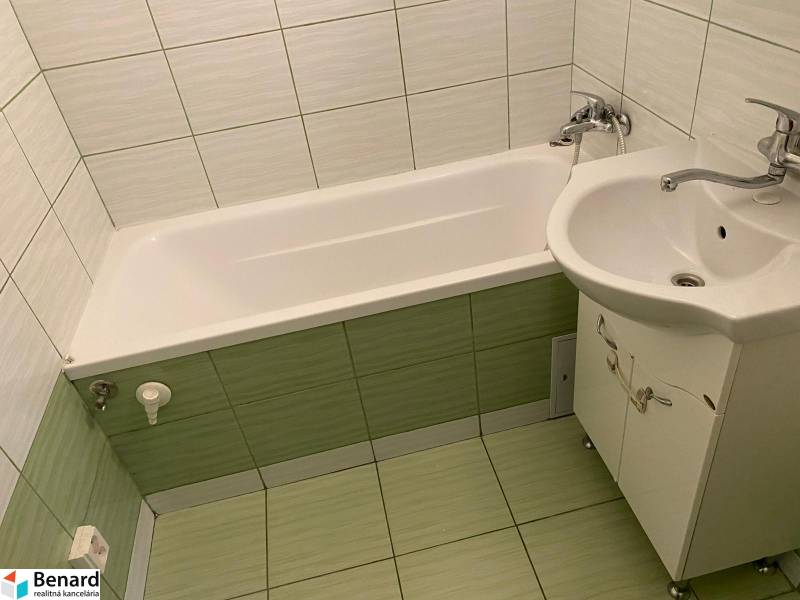 Badezimmer mit Badewanne und Waschbecken in einer 3-Zimmer-Wohnung mit hellen Fliesen und Verkleidungen.