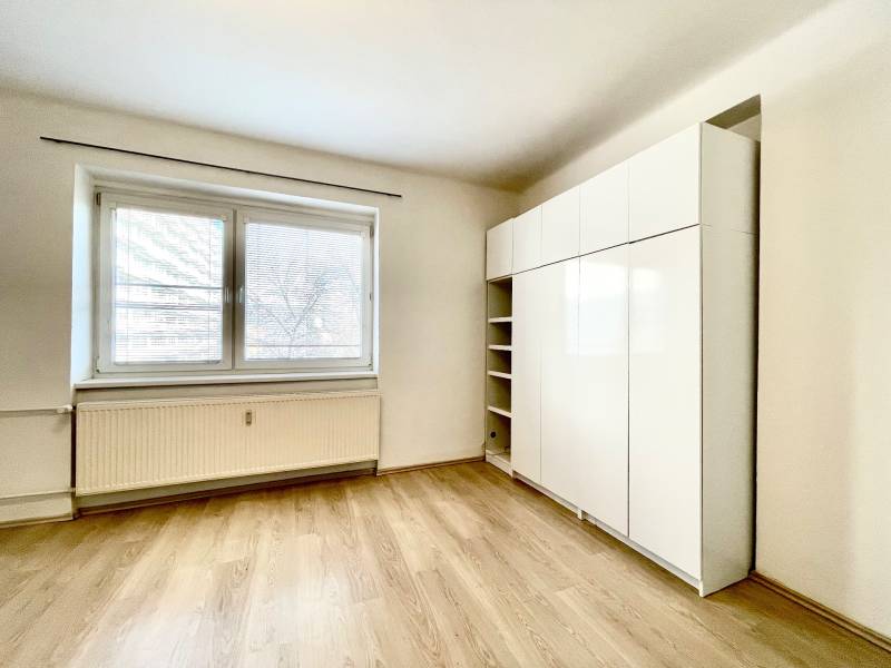 Ein Zimmer mit einem großen Fenster, einem Schrank und einem Boden mit Holzdekor in einer Einzimmerwohnung.
