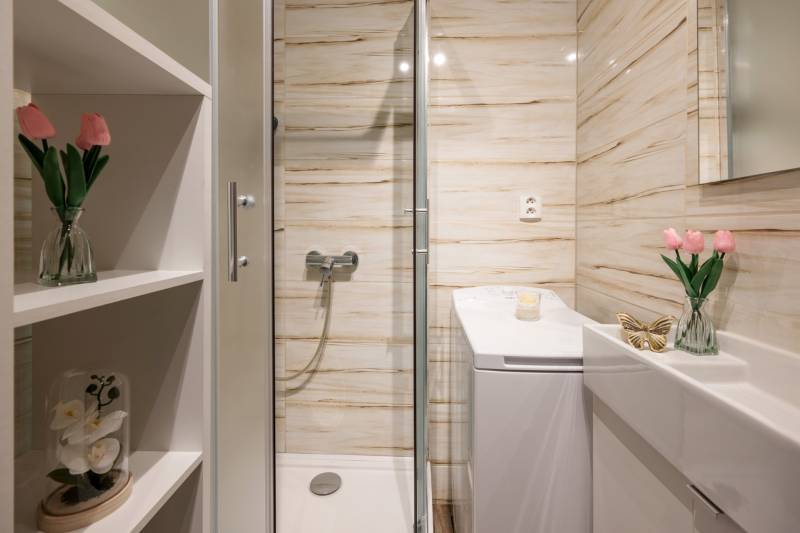 Badezimmer mit Blumen, Duschkabine, Waschbecken und Spiegel in einer Zweizimmerwohnung.