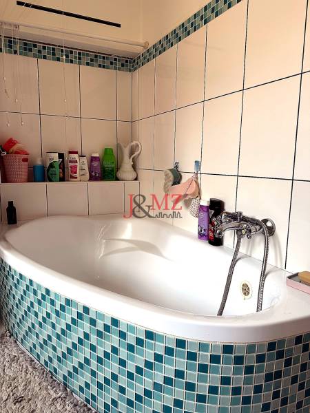 Badezimmer mit Eckbadewanne und blau-weißen Fliesen in einer 2-Zimmer-Wohnung.