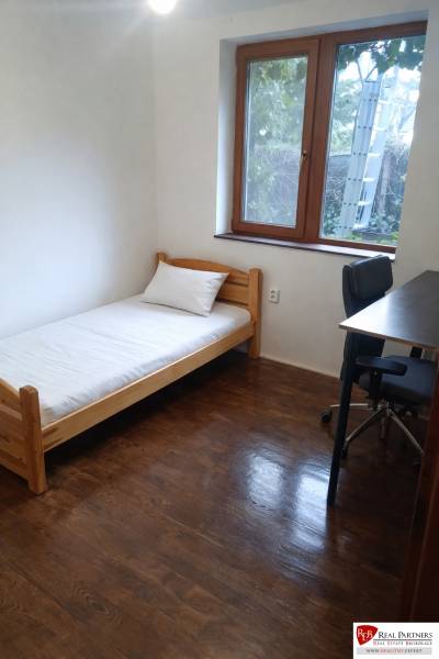 Einfaches Zimmer mit Bett, Tisch und Boden in Holzoptik in einer 3-Zimmer-Wohnung.